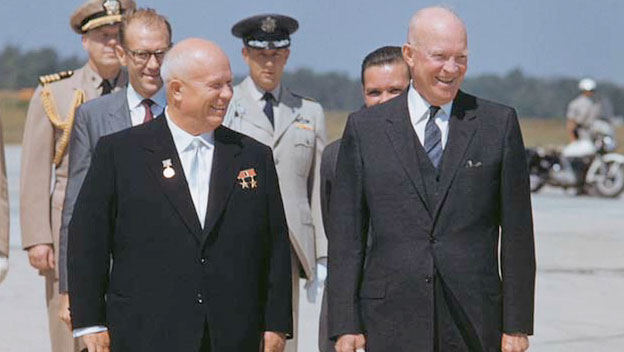 Color photograph of President Dwight D. Eisenhower and Soviet leader Nikita Khrushchev walking side by side. Several men in military uniform stand behind them.